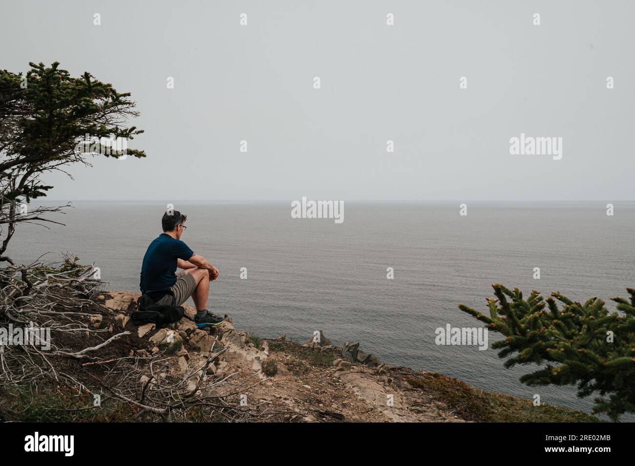 Mann sitzt auf einer felsigen Klippe mit Blick auf das Meer in Neufundland. Stockfoto
