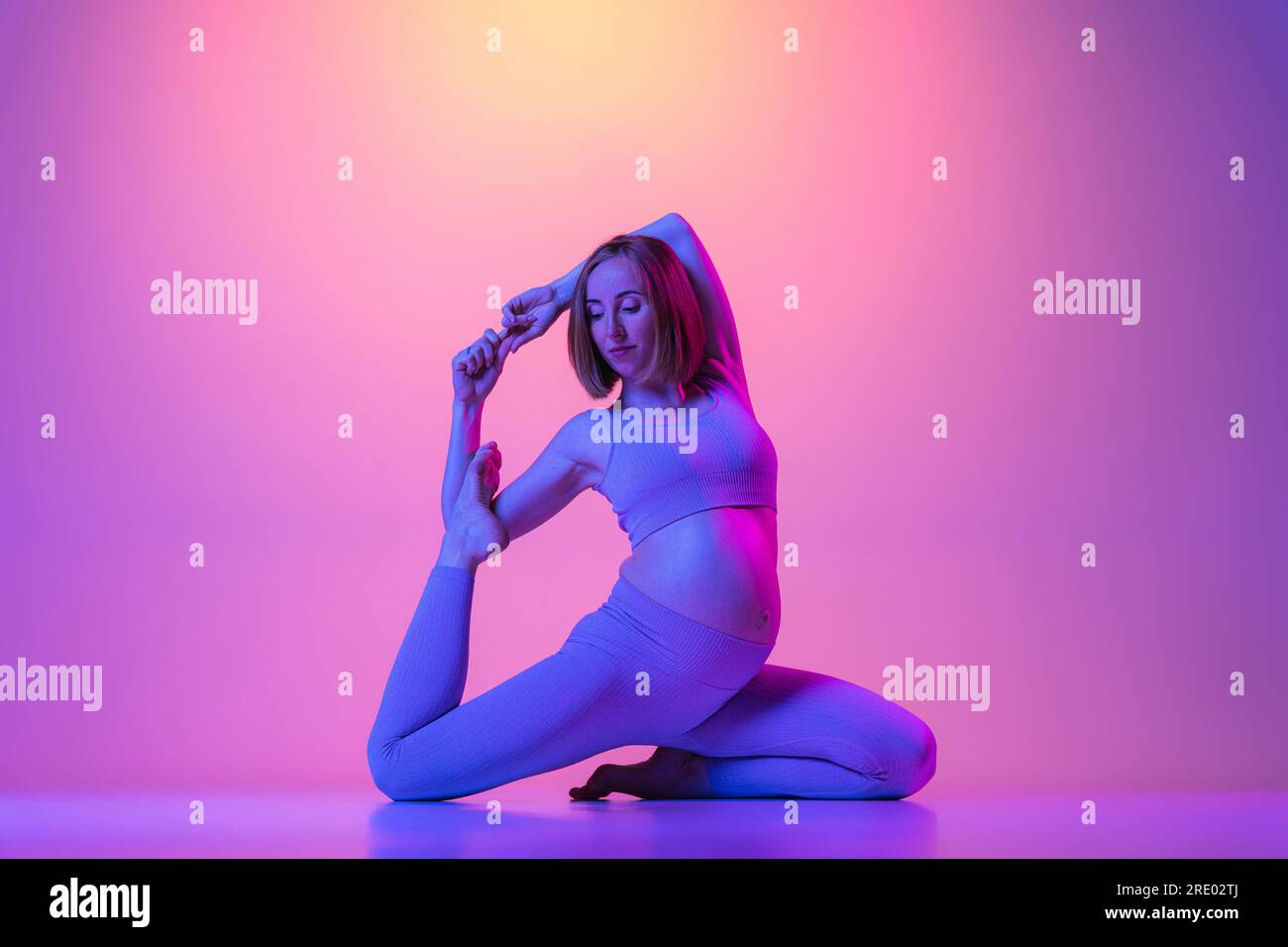 Schwangere Frau, die Beine streckt und Yoga-Übungen in Neon macht Stockfoto