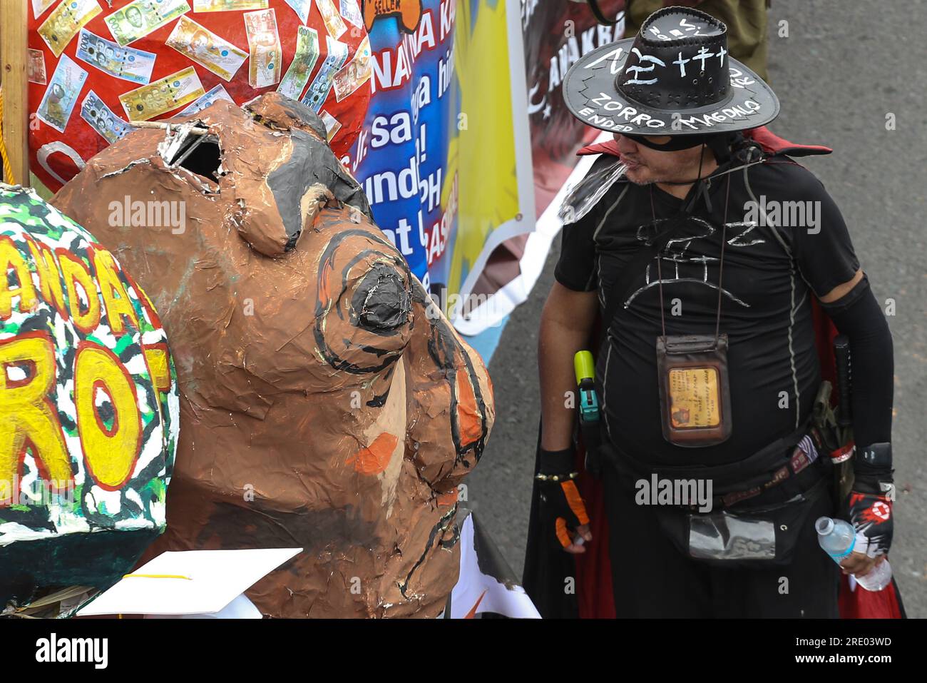 Quezon, Philippinen. 24. Juli 2023. Ein als Zorro verkleideter Demonstrante spuckt Wasser in eine Statue während eines Protestes vor der zweiten Rede des philippinischen Präsidenten Ferdinand Marcos Jr. Ein Protest für das erste Jahr der Marcos-Regierung und für die zweite Rede des Präsidenten zur Lage der Nation. Multisektorale Gruppen, die ihre Anliegen zu verschiedenen sozialen Fragen zum Ausdruck bringen. Kredit: SOPA Images Limited/Alamy Live News Stockfoto
