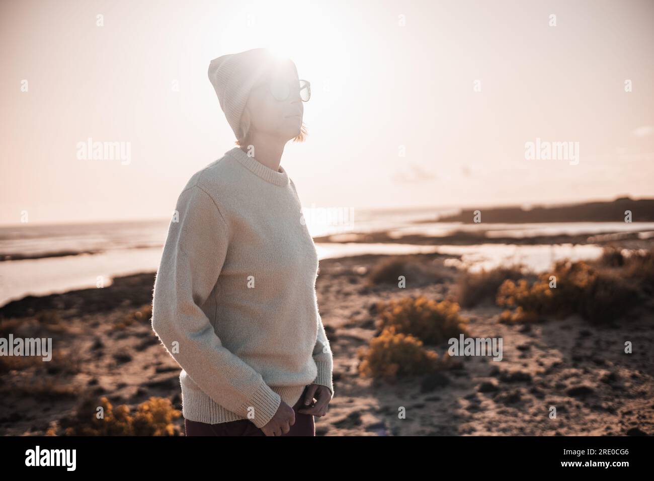 Porträt einer jungen stilvollen Frau mit Wollpullover, Wollmütze und Sonnenbrille am langen Sandstrand im Frühling Stockfoto