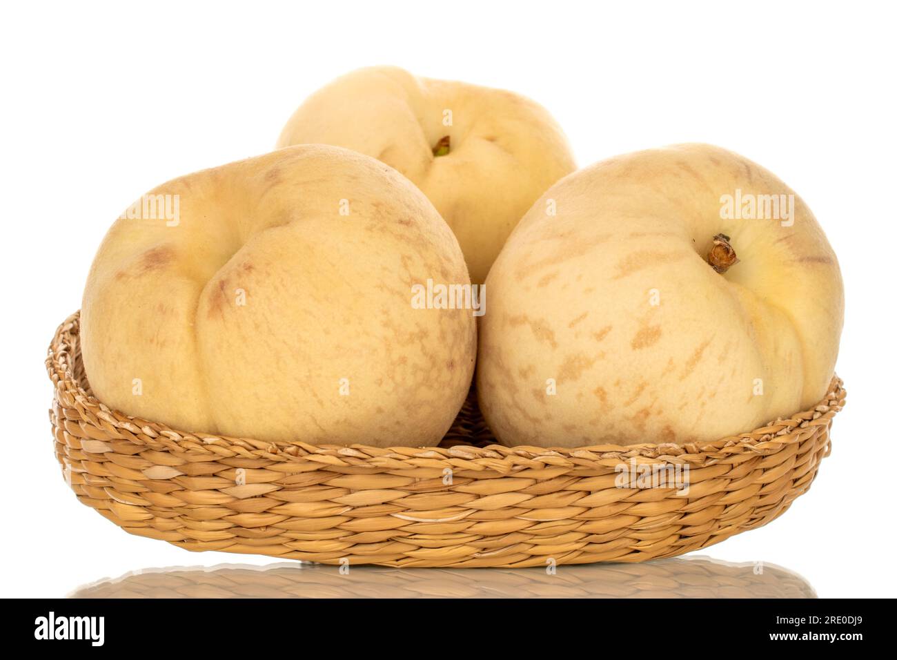 Drei organische reife Pfirsiche auf einer Strohplatte, Makro, isoliert auf weißem Hintergrund. Stockfoto