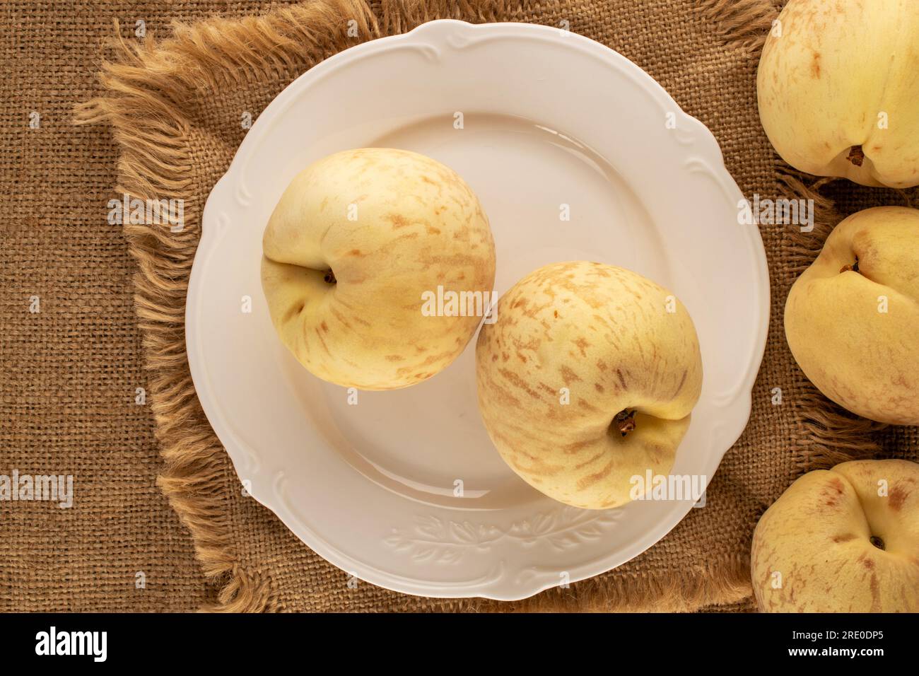 Mehrere organische reife Pfirsiche mit weißer Keramikplatte auf Jutetuch, Makro, Draufsicht. Stockfoto