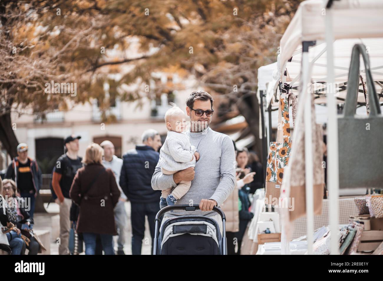 Vater läuft mit seinem kleinen Jungen und schiebt den Kinderwagen in einer Menge Leute, die den sonntagsflohmarkt in Malaga, Spanien, kennen lernen Stockfoto