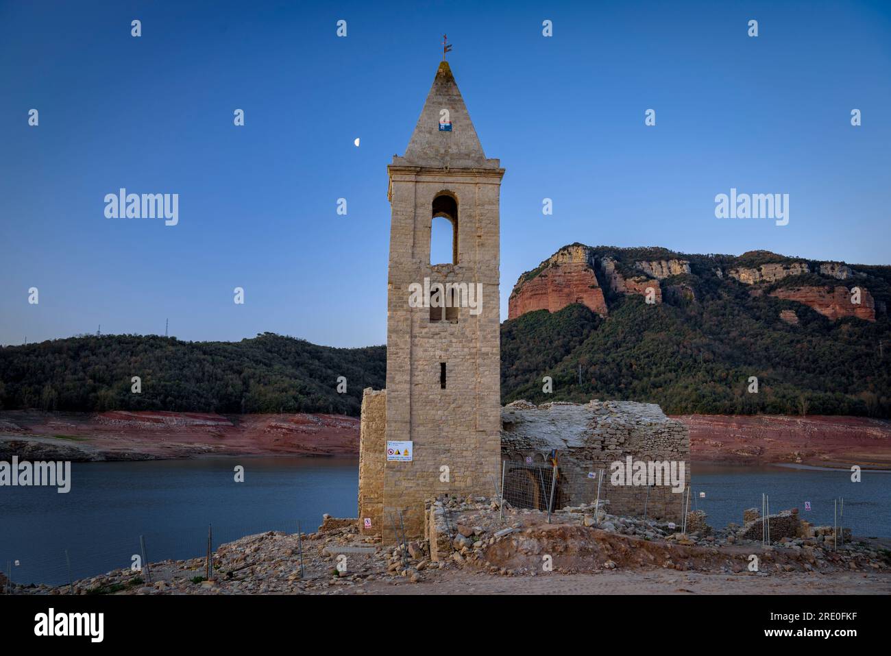 Glockenturm von Sant Romà de Sau bei Sonnenaufgang mit dem sinkenden Mond während der Dürre 2022-23 (Osona, Barcelona, Katalonien, Spanien) Stockfoto