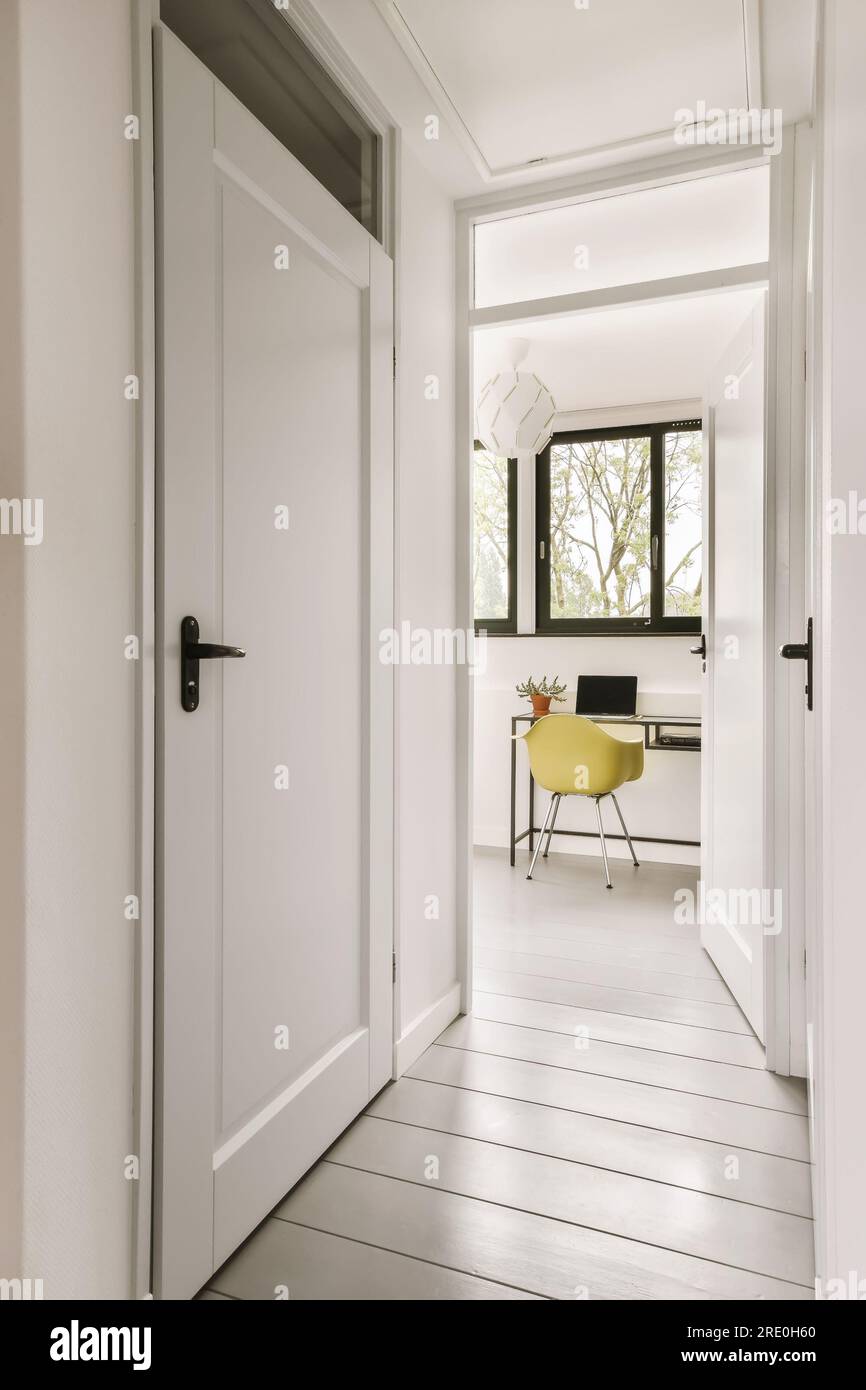 Ein Flur mit weißen Wänden und Holzfußboden. Die Tür führt zu einem Bürobereich mit gelbem Stuhl Stockfoto