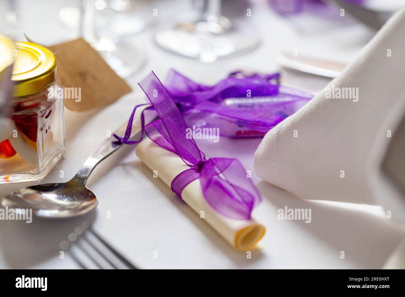 Lila Hochzeitsfavoriten - Süßigkeiten in einer Organza-Tasche, eine Schriftrolle mit Band und Süßigkeiten in einem Glasgefäß Stockfoto