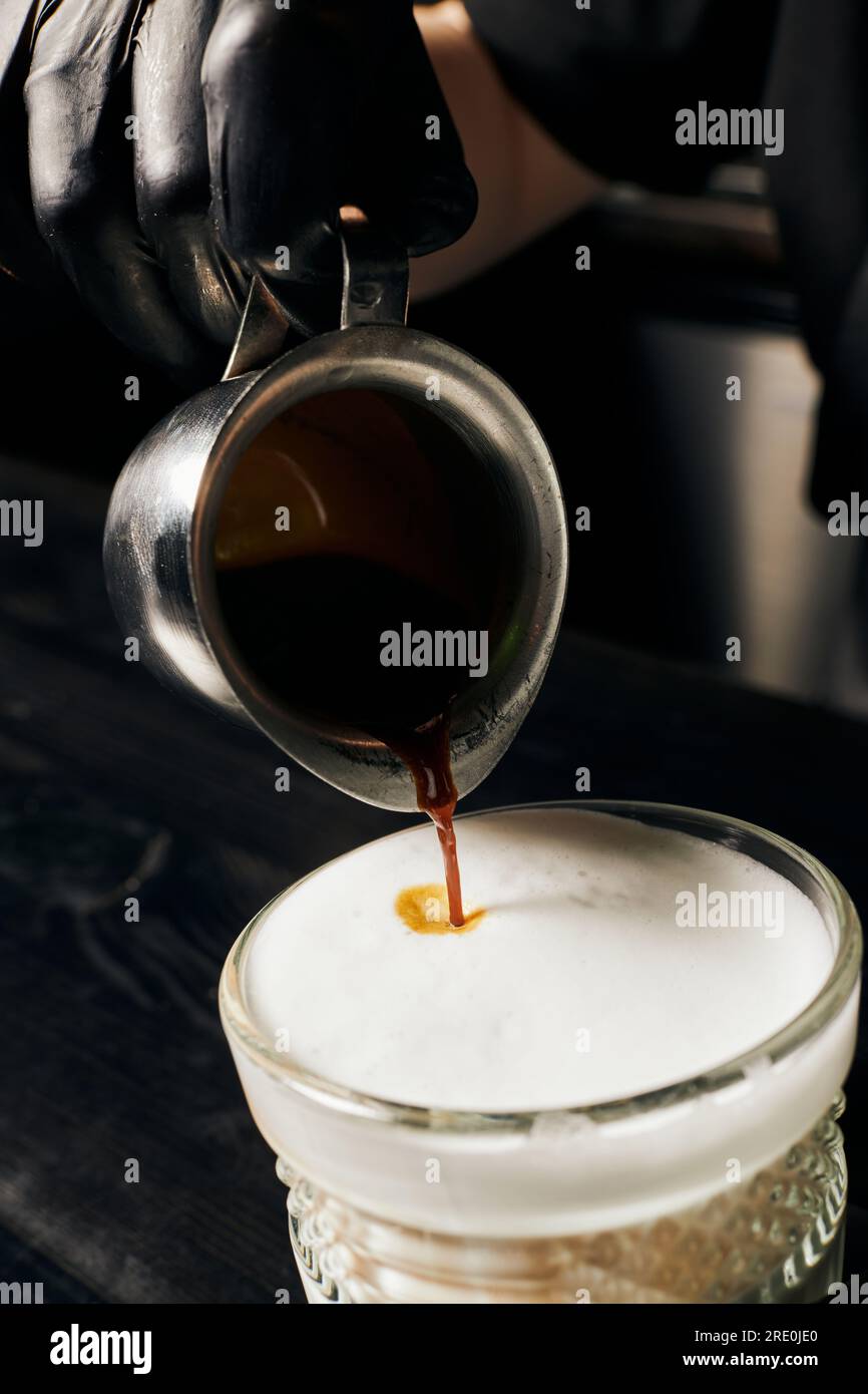 Barista in Latexhandschuhen bereitet Latte Macchiato zu, gießt Espresso ein, Pitcher mit Kaffee, Makro Stockfoto