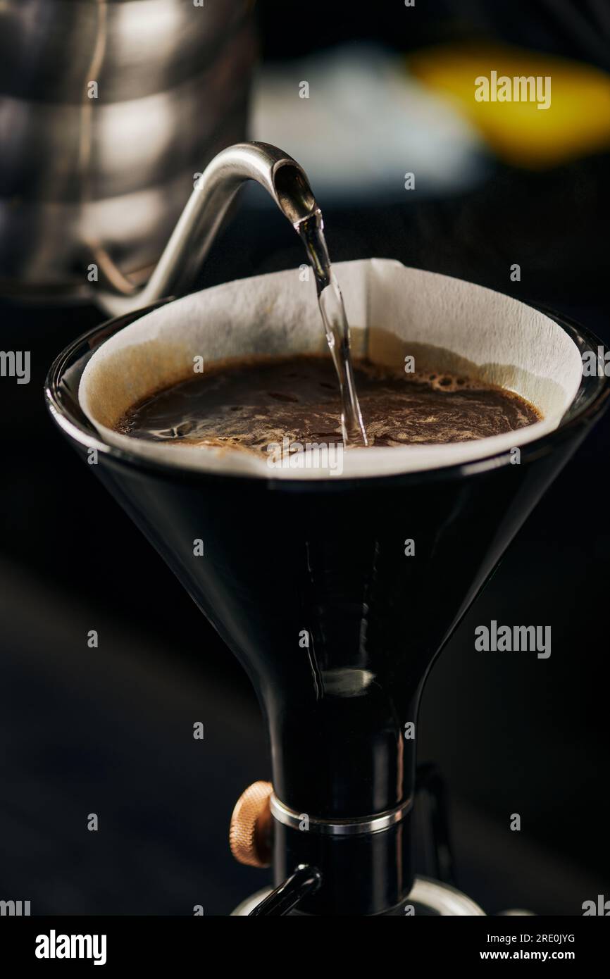 Kochendes Wasser, das aus dem Wasserkocher in die Siphon-Kaffeemaschine mit Papierfilter und Kaffee mit Schaum gefüllt wird Stockfoto