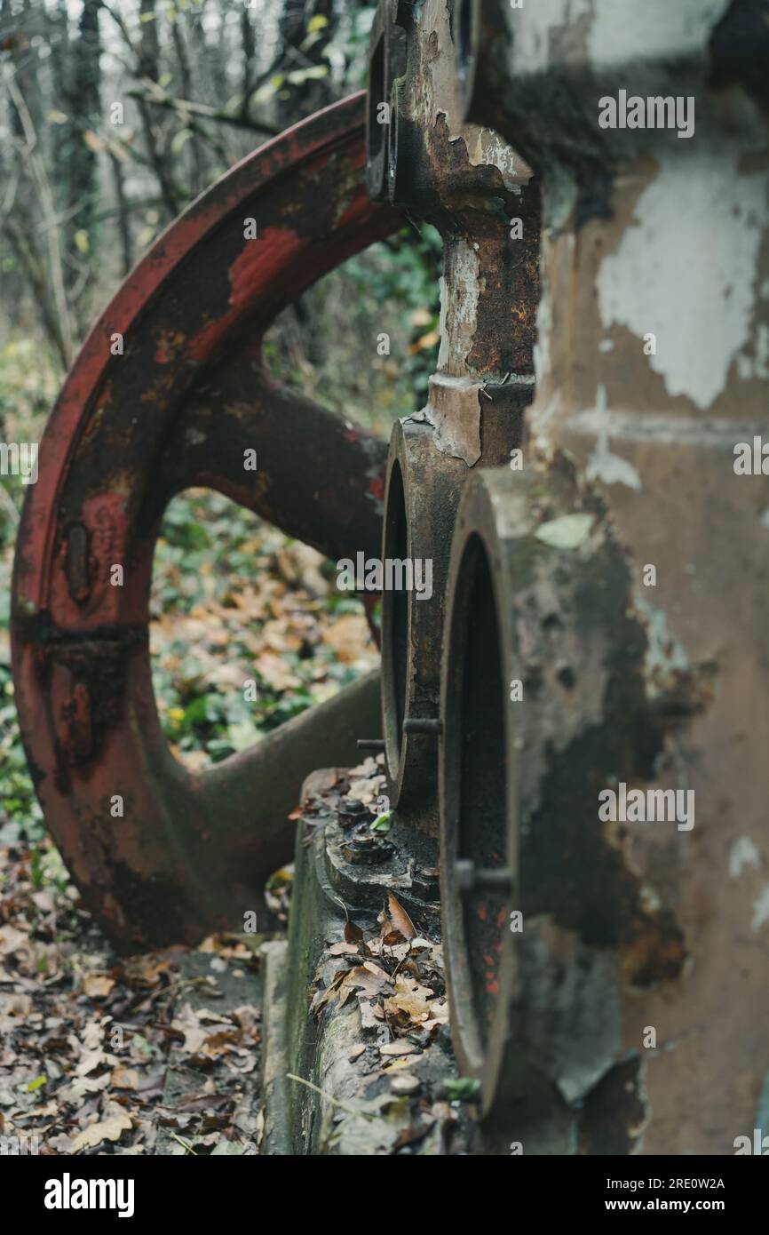 Selektiver Fokus eines alten verrosteten Luftkompressors mit rotem Rad im Wald. Industrielle Geschichtsmaschine. Eisen- und Stahlproduktion. Verlassene Maschine Stockfoto