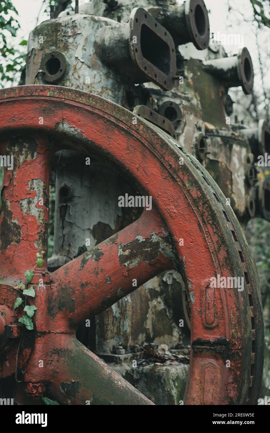 Detail des roten Rads eines alten verrosteten Luftkompressors im Wald. Industrielle Geschichtsmaschine. Eisen- und Stahlproduktion. Verlassene Maschinen. Stockfoto