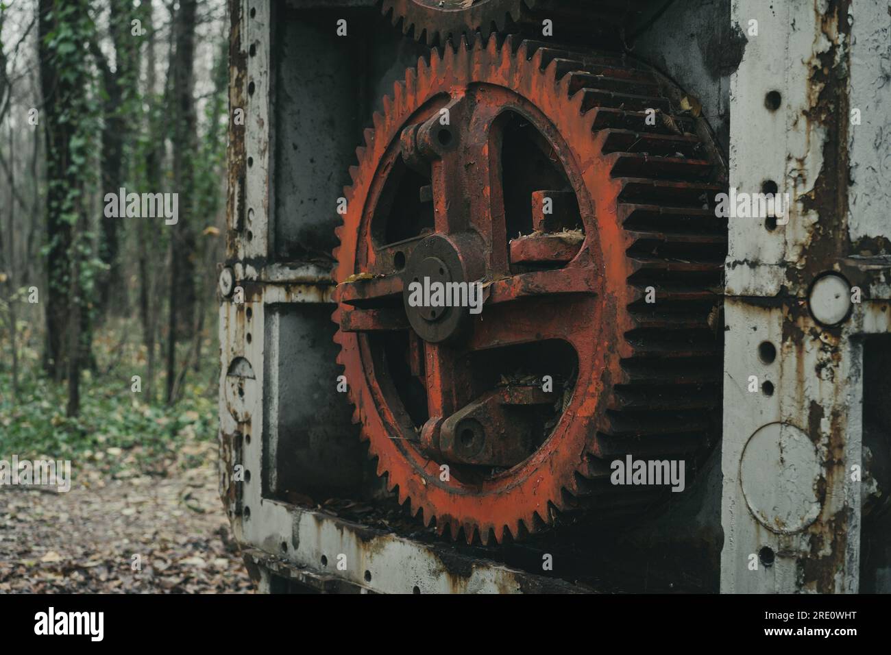 Nahaufnahme des roten Zahnrads einer alten verrosteten, verrosteten Blechbearbeitungsmaschine im Wald. Eisen- und Stahlproduktion. Industrielle Geschichtsmaschine. Stockfoto