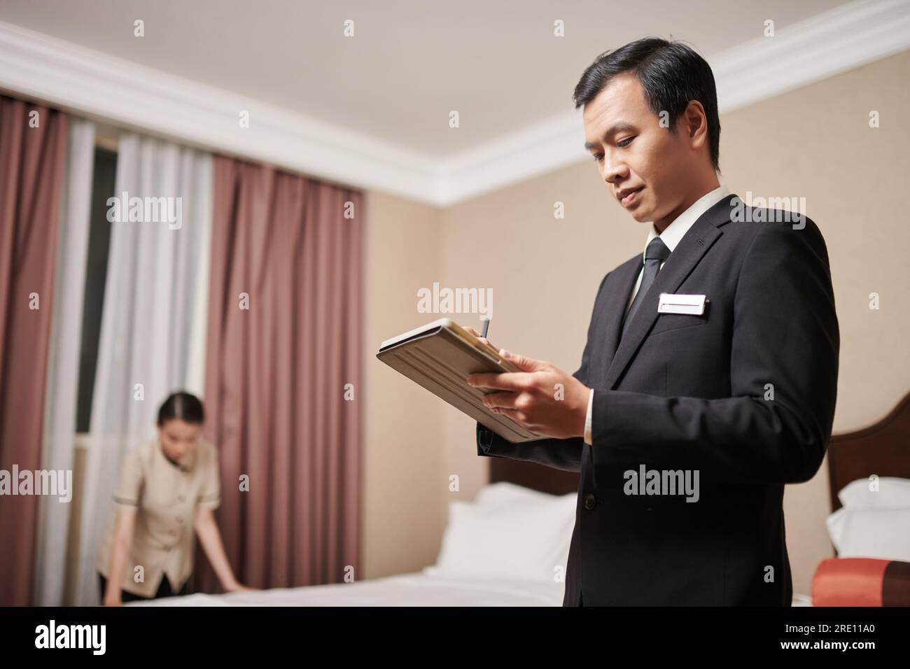 Der Manager des Spa-Resorts unterschreibt das Dokument auf dem Tablet-Computer, wenn das Zimmermädchen das Bett macht Stockfoto