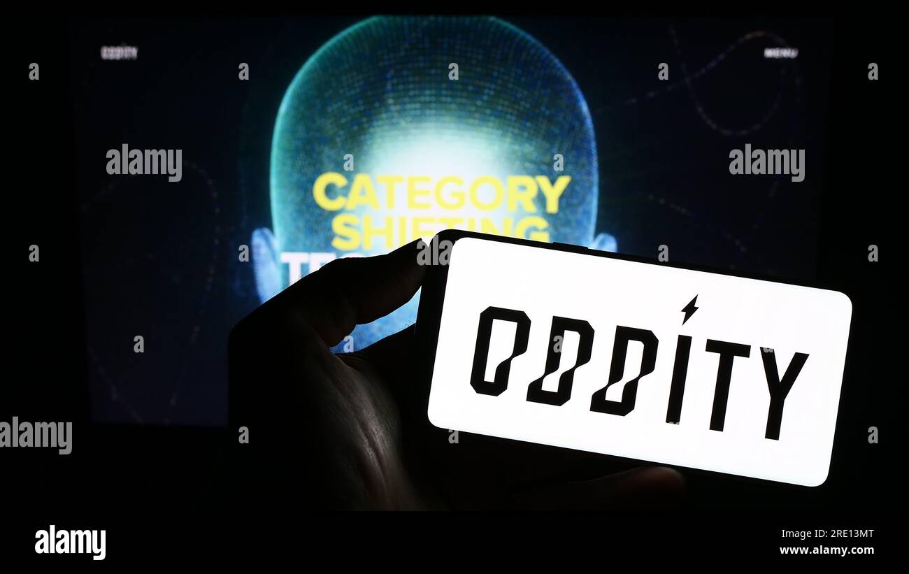 Person, die ein Mobiltelefon mit dem Logo des amerikanischen Technologieunternehmens Oddity Inc. Auf dem Bildschirm vor der Webseite hält. Konzentrieren Sie sich auf das Display des Telefons. Stockfoto