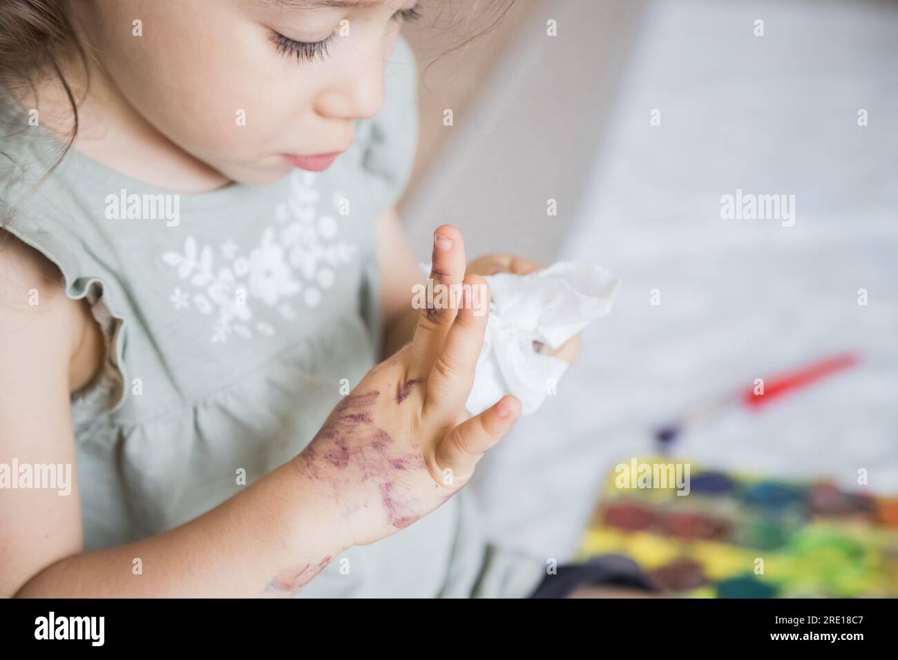 Ein sehr süßes Kind, das sich die Hände putzt, nachdem es mit Aquarellfarben gespielt hat. Konzeptioneller Erwerb von Fertigkeiten, Lernen, Selbstversorgung und Autonomie. Stockfoto