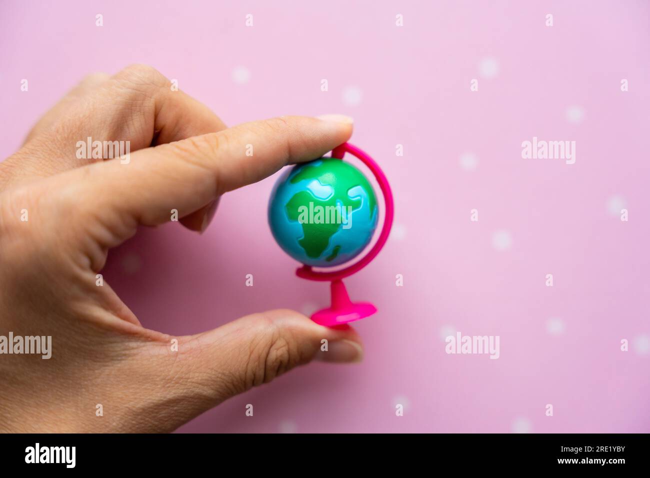 Kleine Spielzeugkugel in Frauenhand auf pinkfarbenem Hintergrund Stockfoto