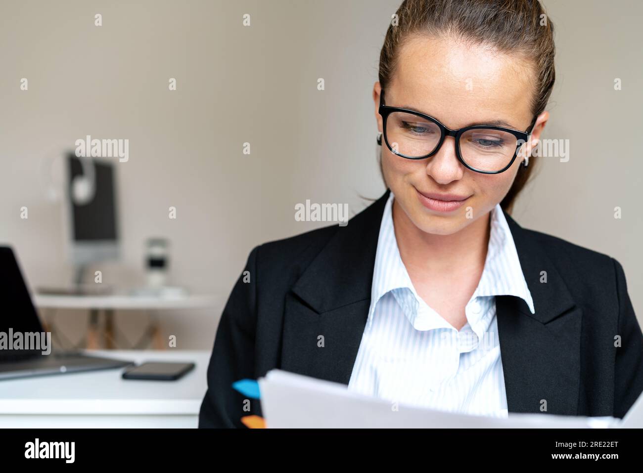 Eine Geschäftsfrau in Anzug und Brille prüft Dokumente, während sie im Büro arbeitet. Stockfoto