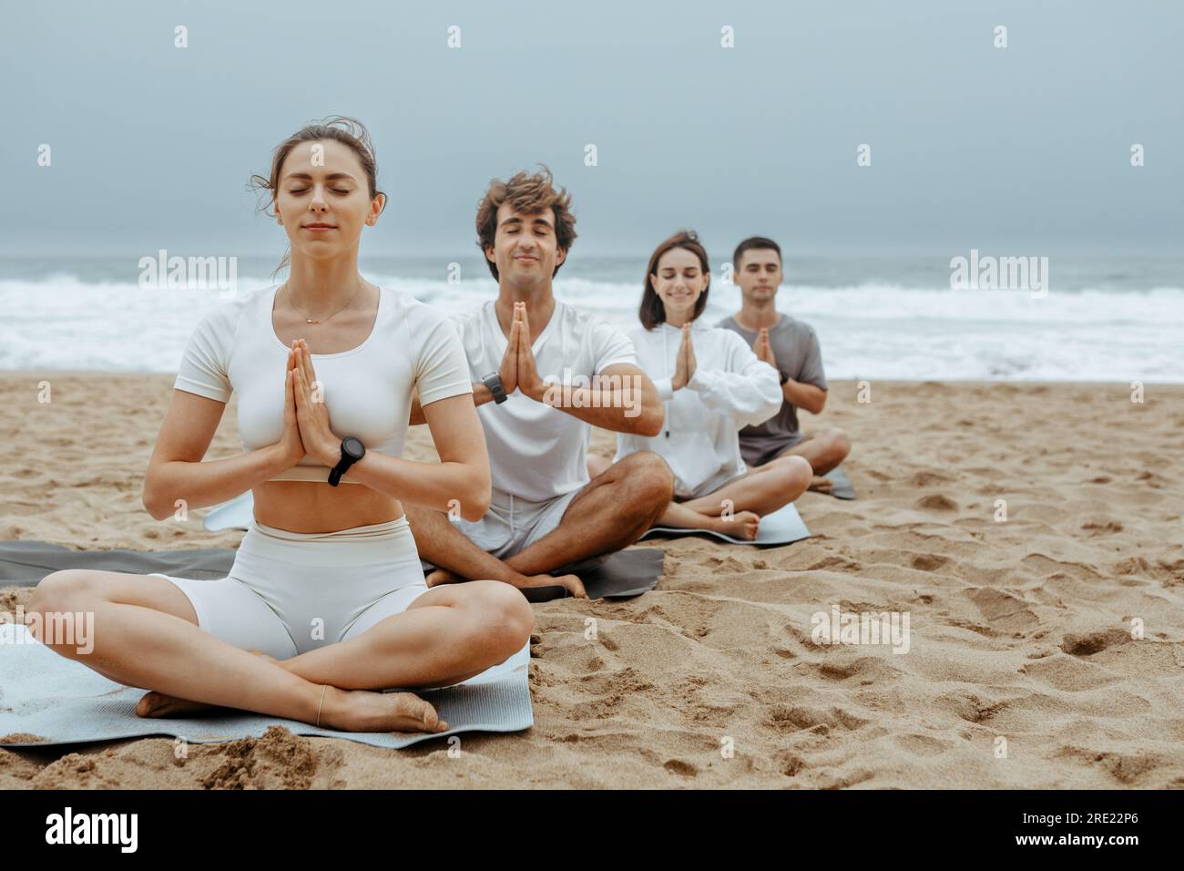 Der Lotus am Strand. Junge Leute meditieren während des Yoga-Kurses im Freien, sitzen auf Matten am Strand Stockfoto