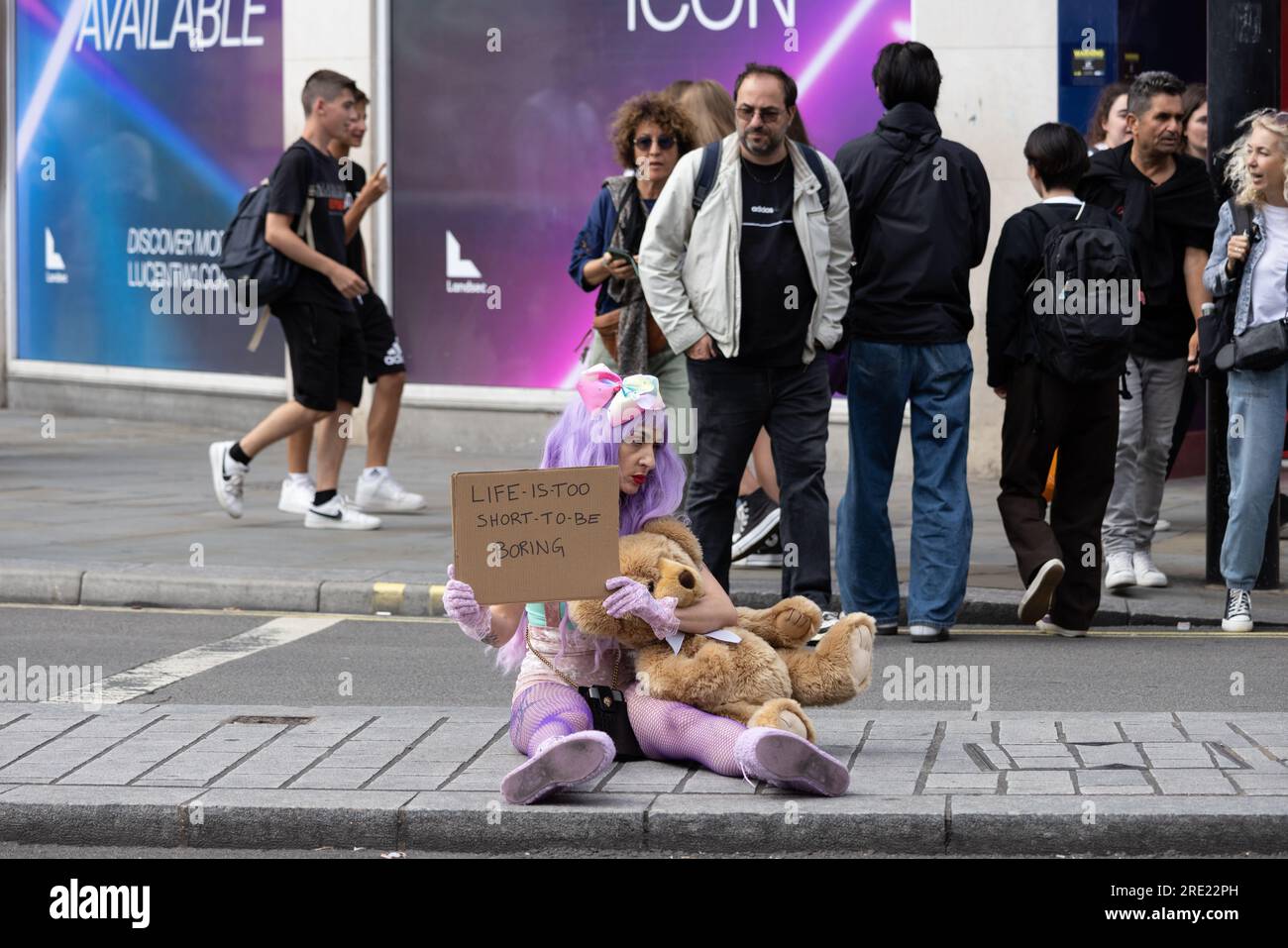 Frau saß auf der Shaftesbury Avenue und hielt ein Plakat mit der Aufschrift "Life is too short to be langweilig", Londons West End, England, Großbritannien Stockfoto