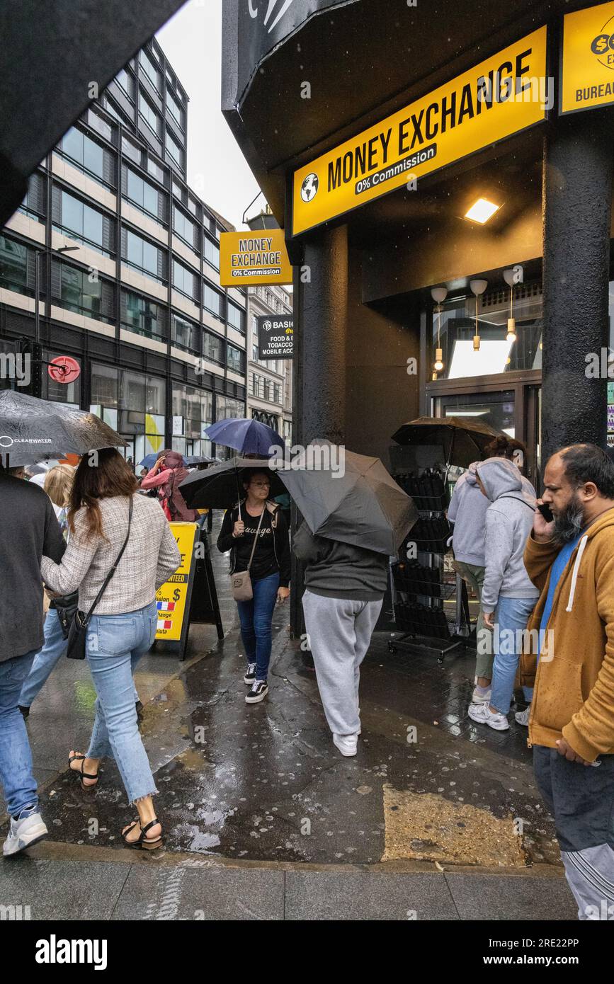 Touristen auf der Oxford Street im Londoner West End können während des Einkaufs in England, Großbritannien, unter den Sonnenschirmen heftige Regenschauer beobachten Stockfoto