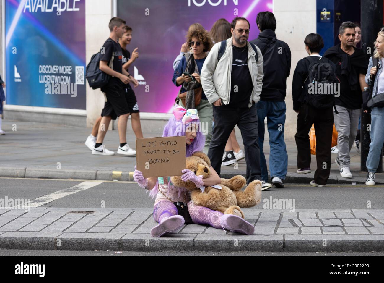 Frau saß auf der Shaftesbury Avenue und hielt ein Plakat mit der Aufschrift "Life is too short to be langweilig", Londons West End, England, Großbritannien Stockfoto