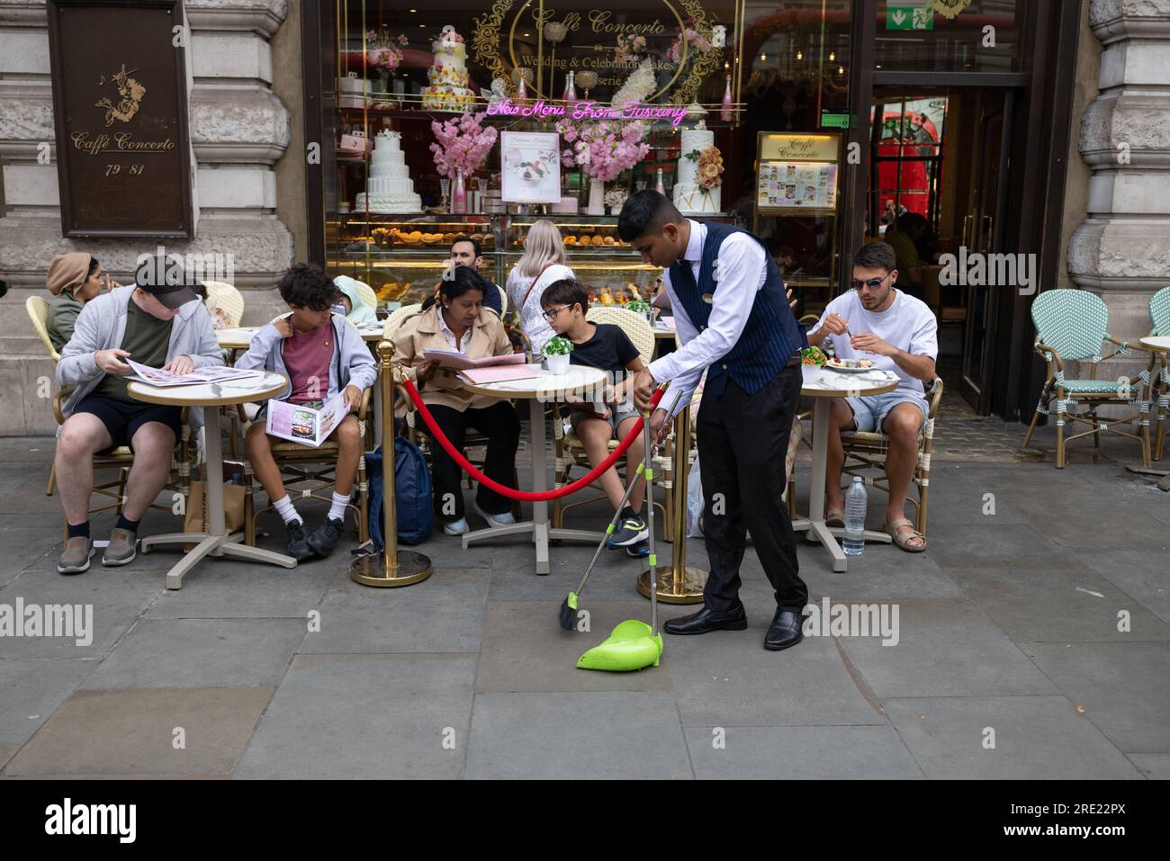 Ein Kellner putzt den Bürgersteig vor einem Café Concerto im Londoner West End, während Touristen diesen Sommer, den 16. Juli 2023, in England, in die Hauptstadt zurückkehren. Stockfoto