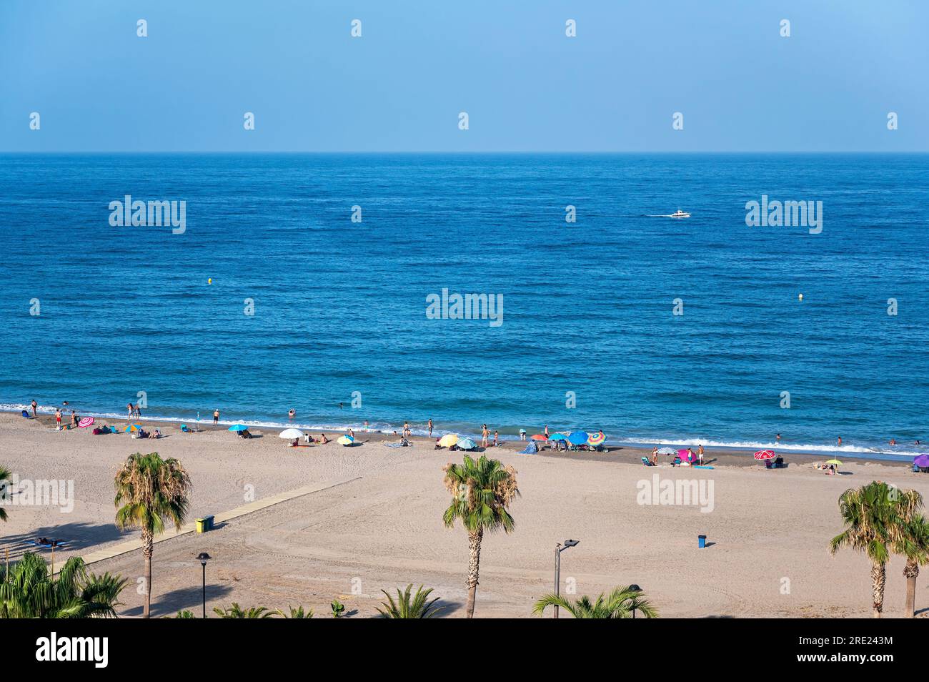 Mojacar, Almeria. Spanien; 07-13-2023: Leute, die einen Tag am Strand genießen, Leute mit Sonnenschirmen an der Küste, andere baden, ein Boot segeln und kumpel Stockfoto