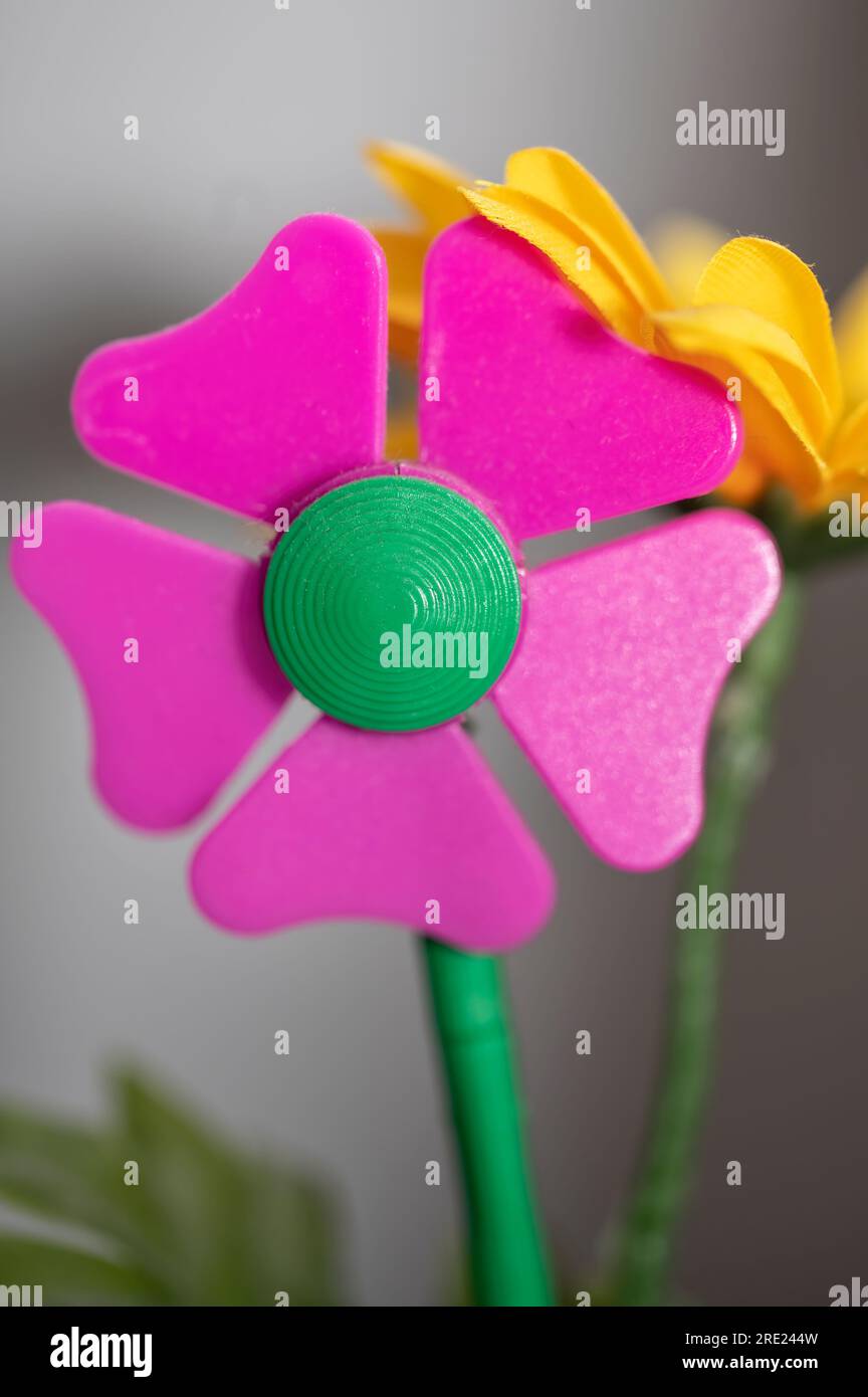 Nahaufnahme einer rosa Blume aus Kunststoff mit einer gelben Blume aus Stoff dahinter Stockfoto