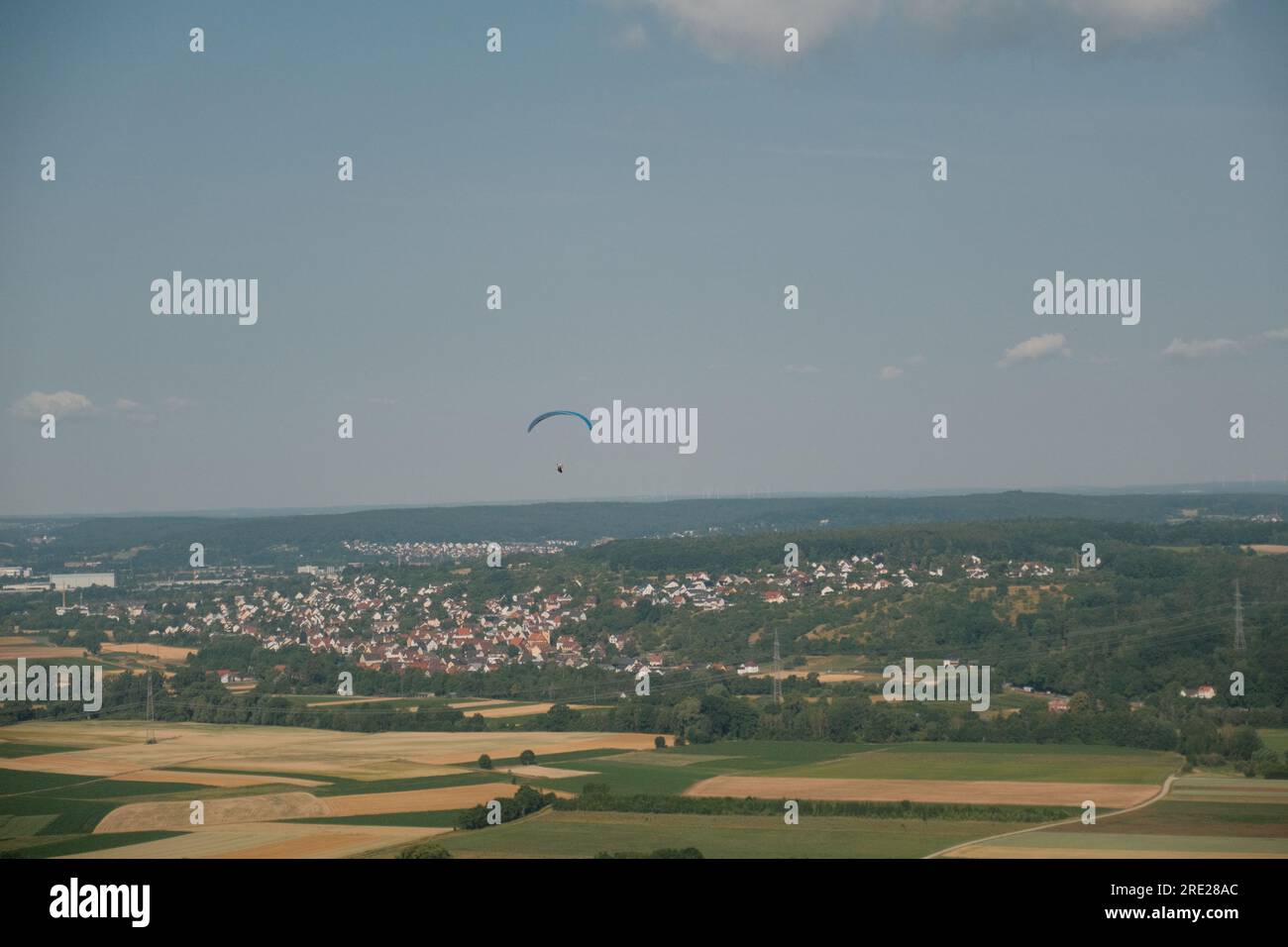 Ein Abenteurer gleitet inmitten des offenen Himmels und bietet einen fesselnden Blick auf die ruhige deutsche Landschaft und die entfernte Stadt darunter. Stockfoto