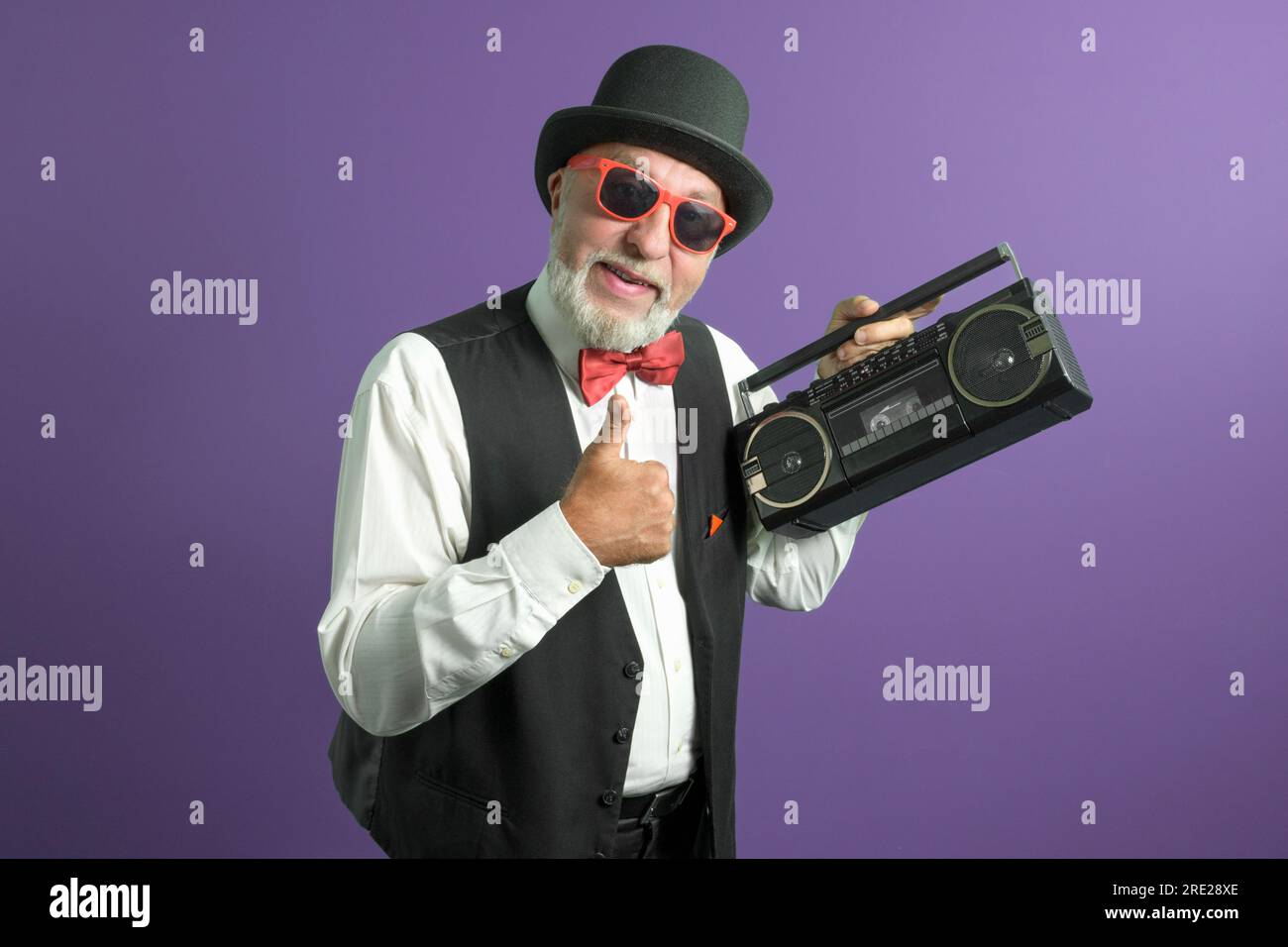 Tolle 80s. Ein älterer Mann in einem alten klassischen Anzug mit einem Kassettenrekorder auf lila Hintergrund. Stockfoto