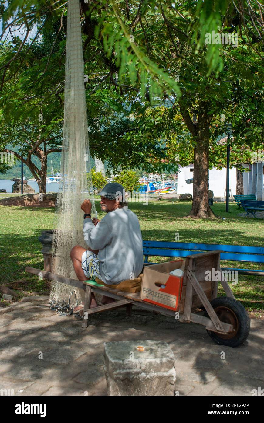 Engagierter Fischer, der Fischernetze auf dem Platz repariert, ein Einblick in das authentische Leben an der Küste in Rio de Janeiro, Brasilien Stockfoto