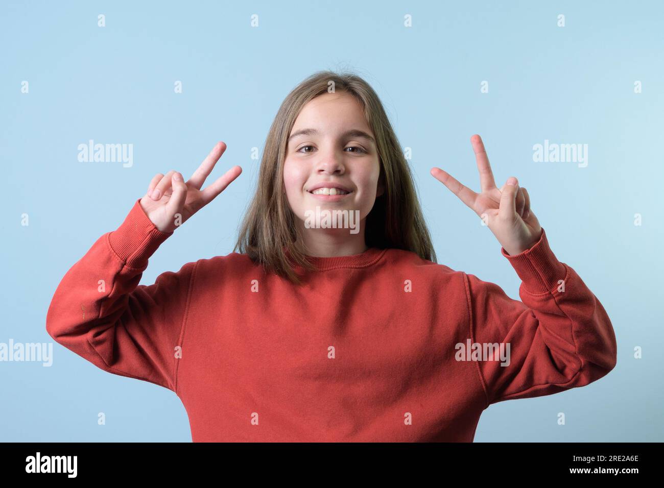 Ein Teenager macht ein Siegeszeichen mit beiden Händen. Roter Pullover, blauer Hintergrund Stockfoto