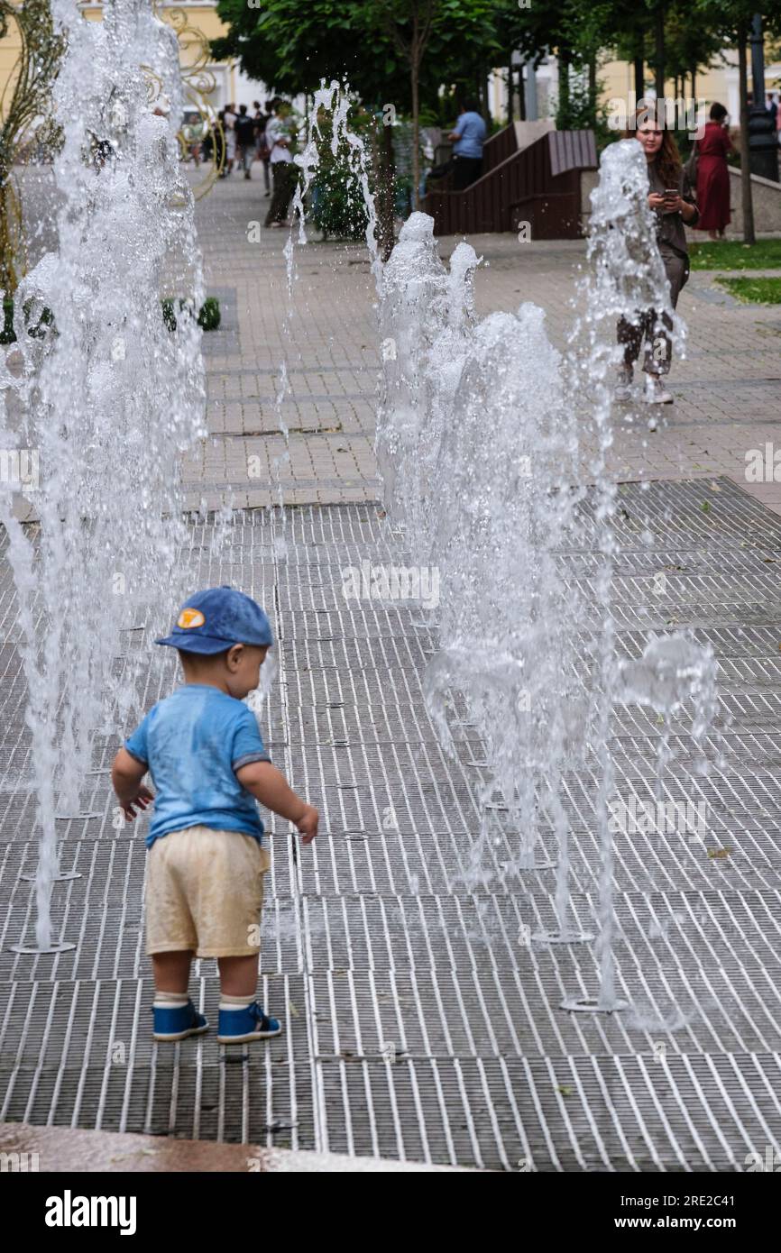Kasachstan, Almaty. Der kleine Kasachisch-Junge erforscht Brunnen auf der Panfilov Promenade, einem Fußgängerweg. Stockfoto