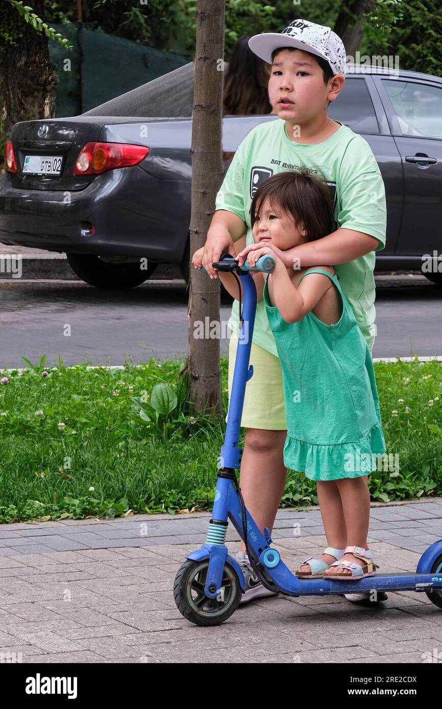 Kasachstan, Almaty. Boy and Little Sister on Scooter auf der Panfilov Promenade, einem Fußgängerweg. Stockfoto