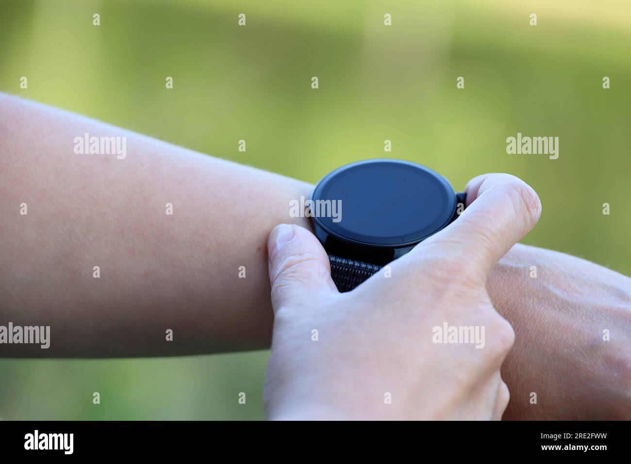 Intelligente Uhr auf weiblicher Hand im Sommerpark. Rundes Display mit Apps für Wandern und Sporttraining Stockfoto