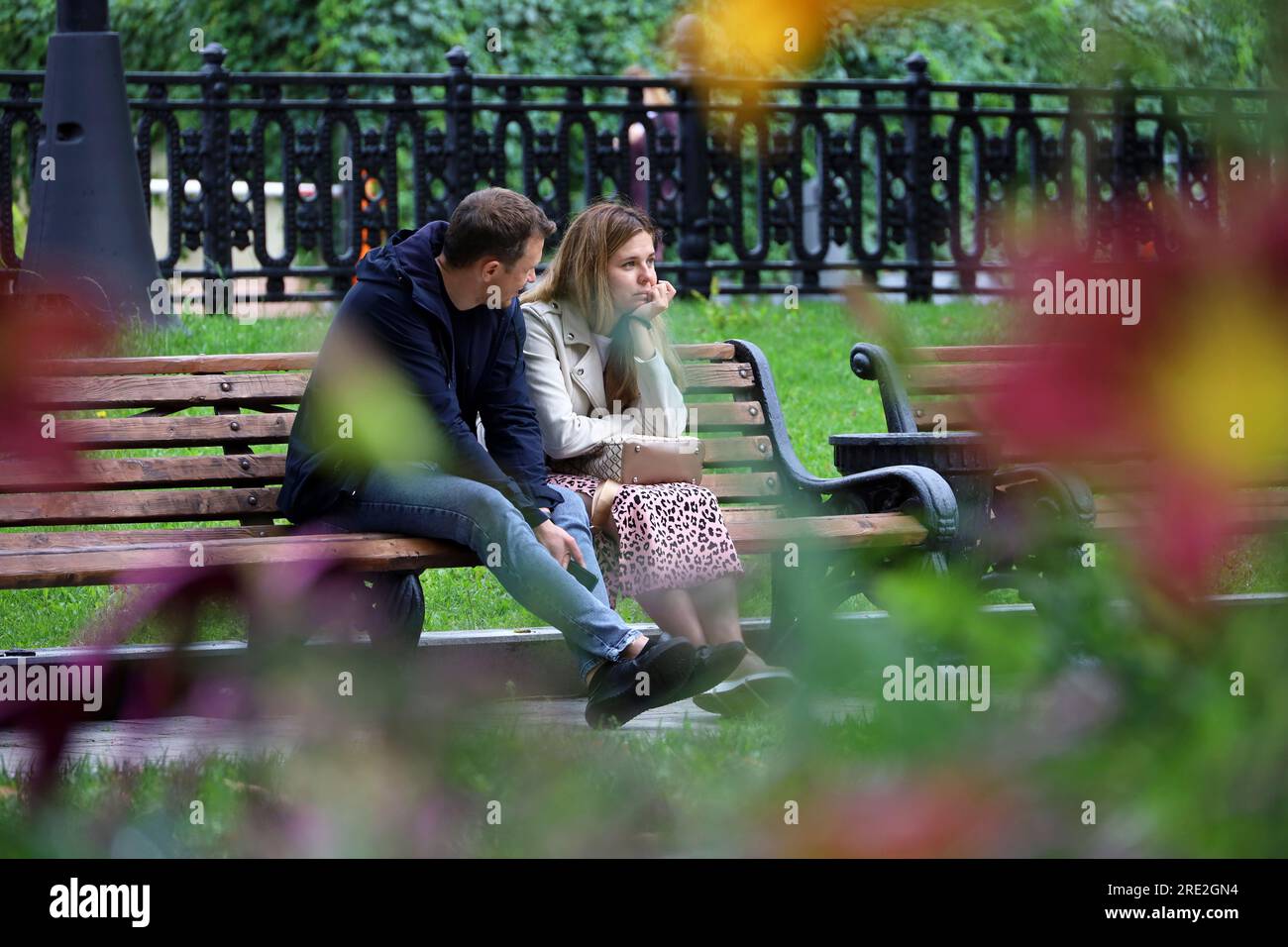 Ein Paar sitzt auf einer Holzbank im Sommerpark und blickt durch die Blumen Stockfoto