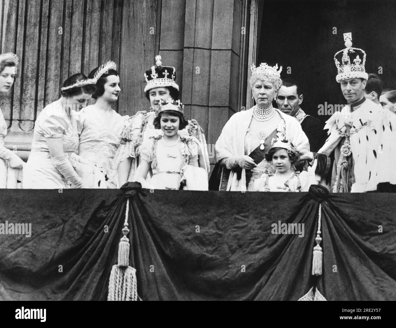 London, England: 12. Mai, 1937 King George VI. Und Queen Elizabeth am Krönungstag auf dem Balkon des Buckingham Palace. In der Mitte befindet sich Queen Mary und vorne sind Prinzessin Elizabeth (links) und Prinzessin Margaret Rose, deren übergroße Krone von König George aufgehalten wird. Rechts von Königin Elizabeth ist Lady Ursula Manners, eine ihrer sechs Ausbilder. Stockfoto