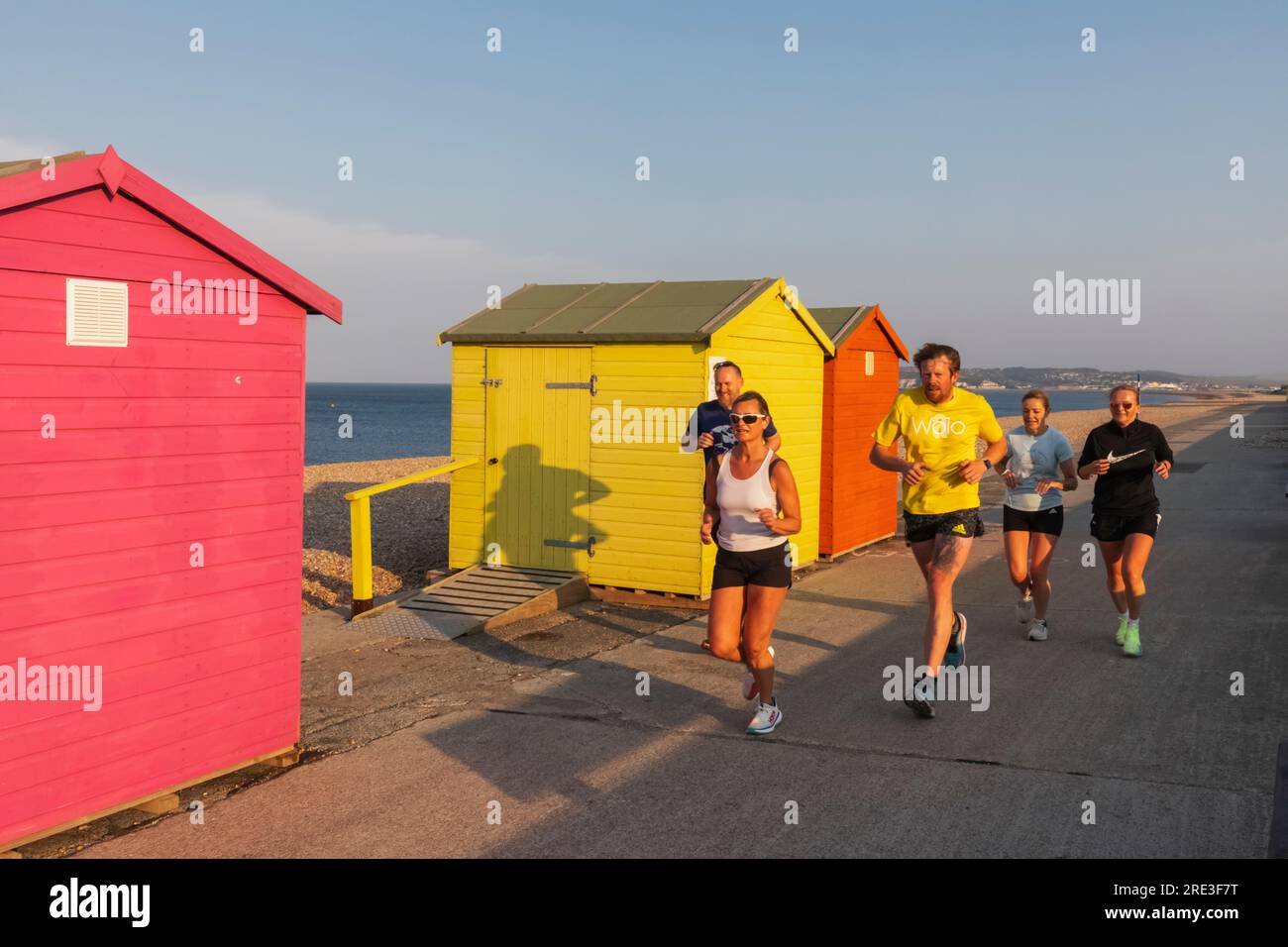 England, Sussex, East Sussex, Seaford, bunte Strandhütten am Meer und Jogger am frühen Morgen Stockfoto