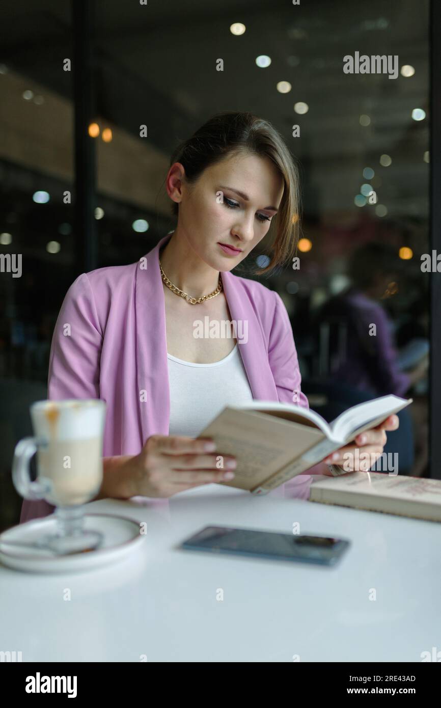 Junge, süße weiße Frau, die ein Buch in einem Café liest, Kopierraum, vertikal Stockfoto