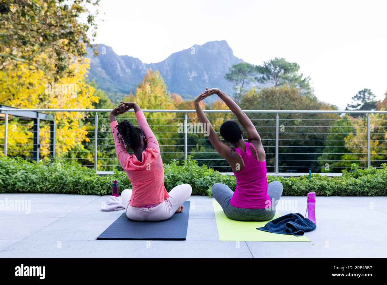 Rücken von afroamerikanischer Mutter und Tochter, die zu Hause Yoga auf der sonnigen Terrasse praktizieren Stockfoto