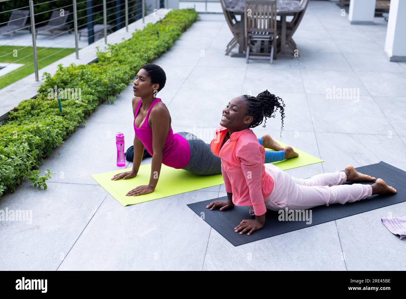 Glückliche afroamerikanische Mutter und Tochter, die zu Hause Yoga auf der sonnigen Terrasse praktizieren Stockfoto