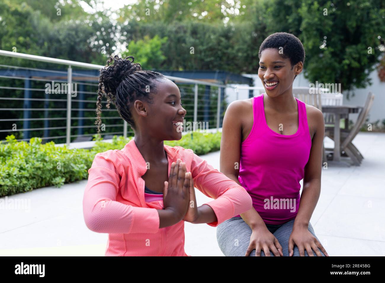 Glückliche afroamerikanische Mutter und Tochter, die zu Hause Yoga auf der sonnigen Terrasse praktizieren Stockfoto