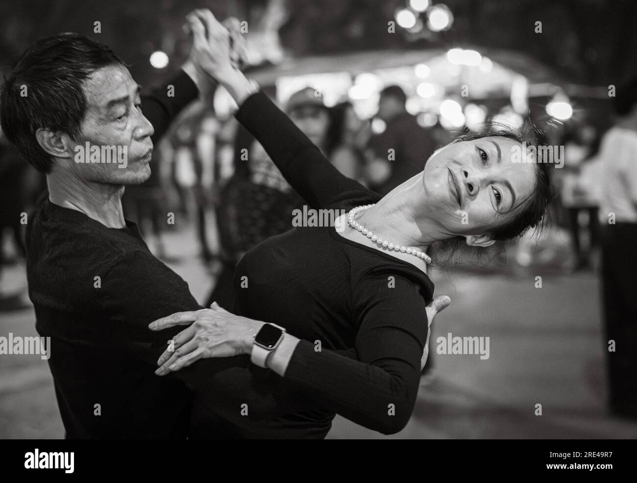 Ein vietnamesisches Paar mittleren Alters, das nachts in schwarz gekleideten Straßen neben dem Hoan Kiem See im Zentrum von Hanoi, Vietnam, tanzt. Stockfoto