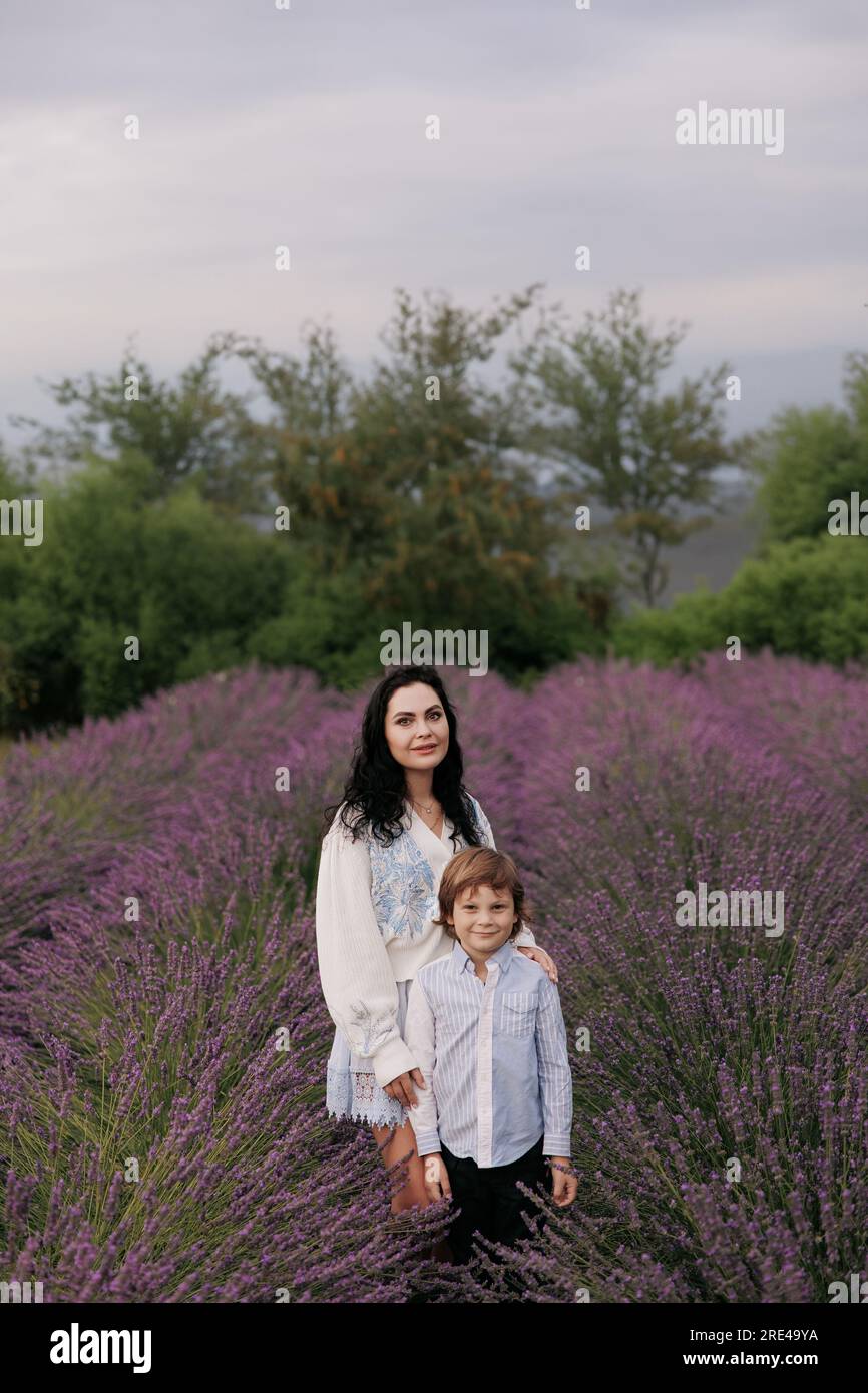 Lächelnde Mutter und Sohn, die zwischen blühenden Lavendelreihen vor dem Hintergrund des Himmels spazieren. Stockfoto