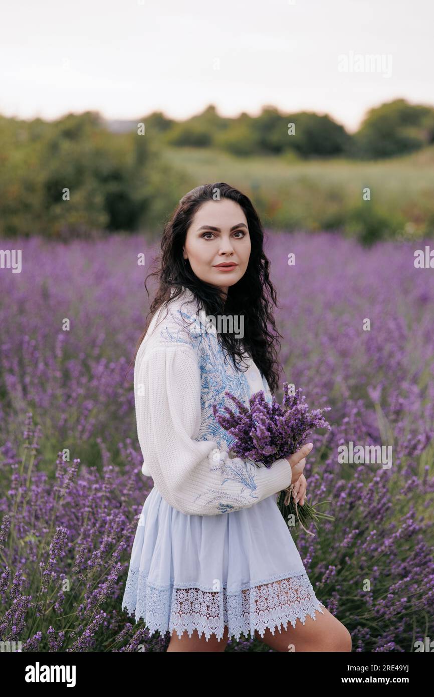 Junge brünette Frau, die mit einem Lavendelstrauß in den Händen vor dem Hintergrund eines blühenden Lavendelfeldes spaziert. Nahaufnahme. Stockfoto