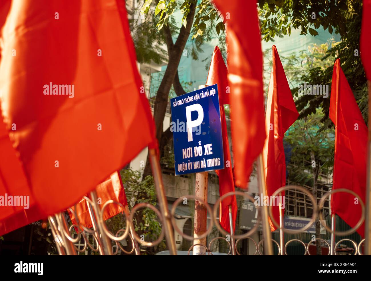 Kommunistische rote Flaggen, die ein blaues Schild mit dem Buchstaben „P“ umgeben, um auf einen offiziellen Parkplatz in einer Straße in Hanoi, Vietnam, hinzuweisen. Stockfoto