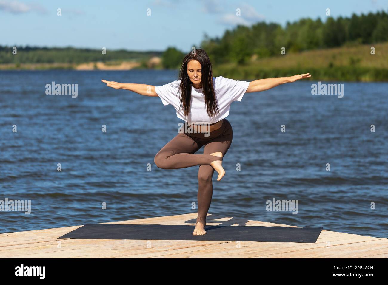 Yoga-Praktizierende Frau, führt die Übung Eka Pada Agnistambha Utkatasana durch, balanciert Asana, trainiert Sportbekleidung, während sie auf einem Bein auf einem Woode steht Stockfoto