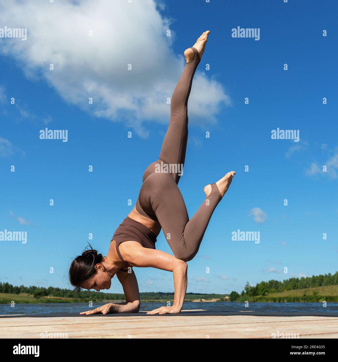 Eine Frau, die Yoga praktiziert, führt die Übung Eka Pada Bakasana durch, die Pose eines Krans mit ausgestrecktem Bein, trainiert in Sportbekleidung, während sie auf h steht Stockfoto
