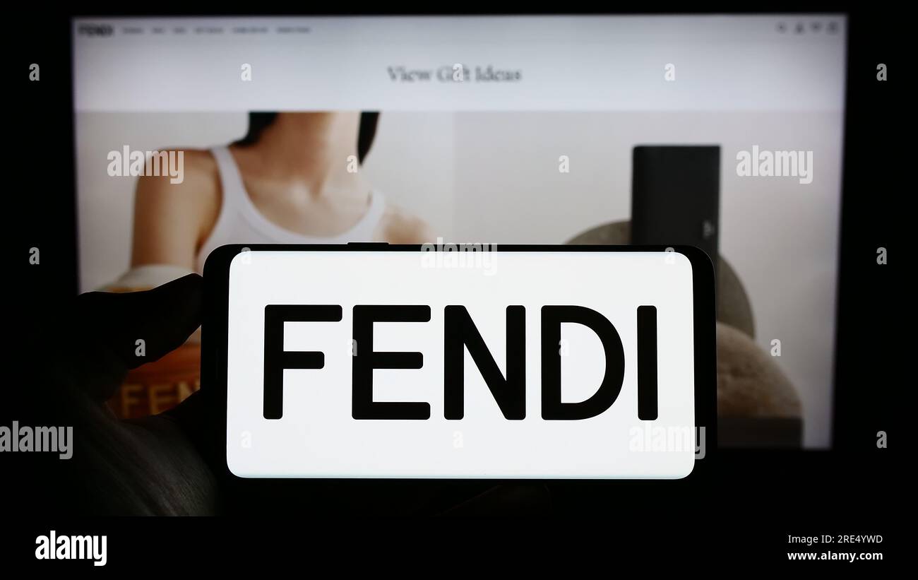 Person, die ein Handy mit dem Logo des italienischen Modeunternehmens Fendi S.r.l. auf dem Bildschirm vor der Business-Webseite hält. Konzentrieren Sie sich auf das Display des Telefons. Stockfoto