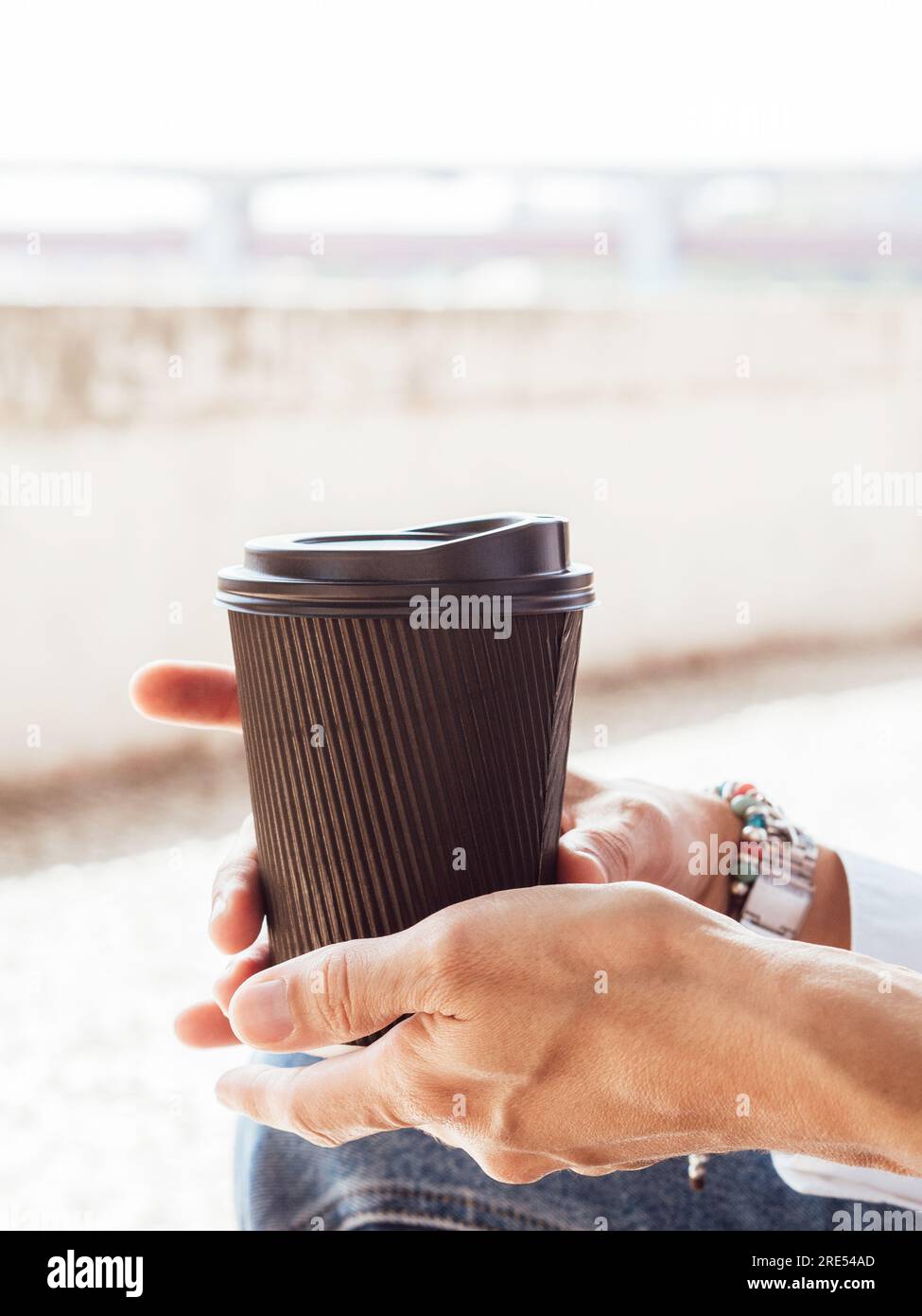 Kaffeetasse aus schwarzem Papier in der Hand auf unscharfem Hintergrund aus der Stadt. Die Hände von Famale halten einen Einwegbecher mit schwarzem Deckel. Werbung für Latte oder Tee. Stockfoto
