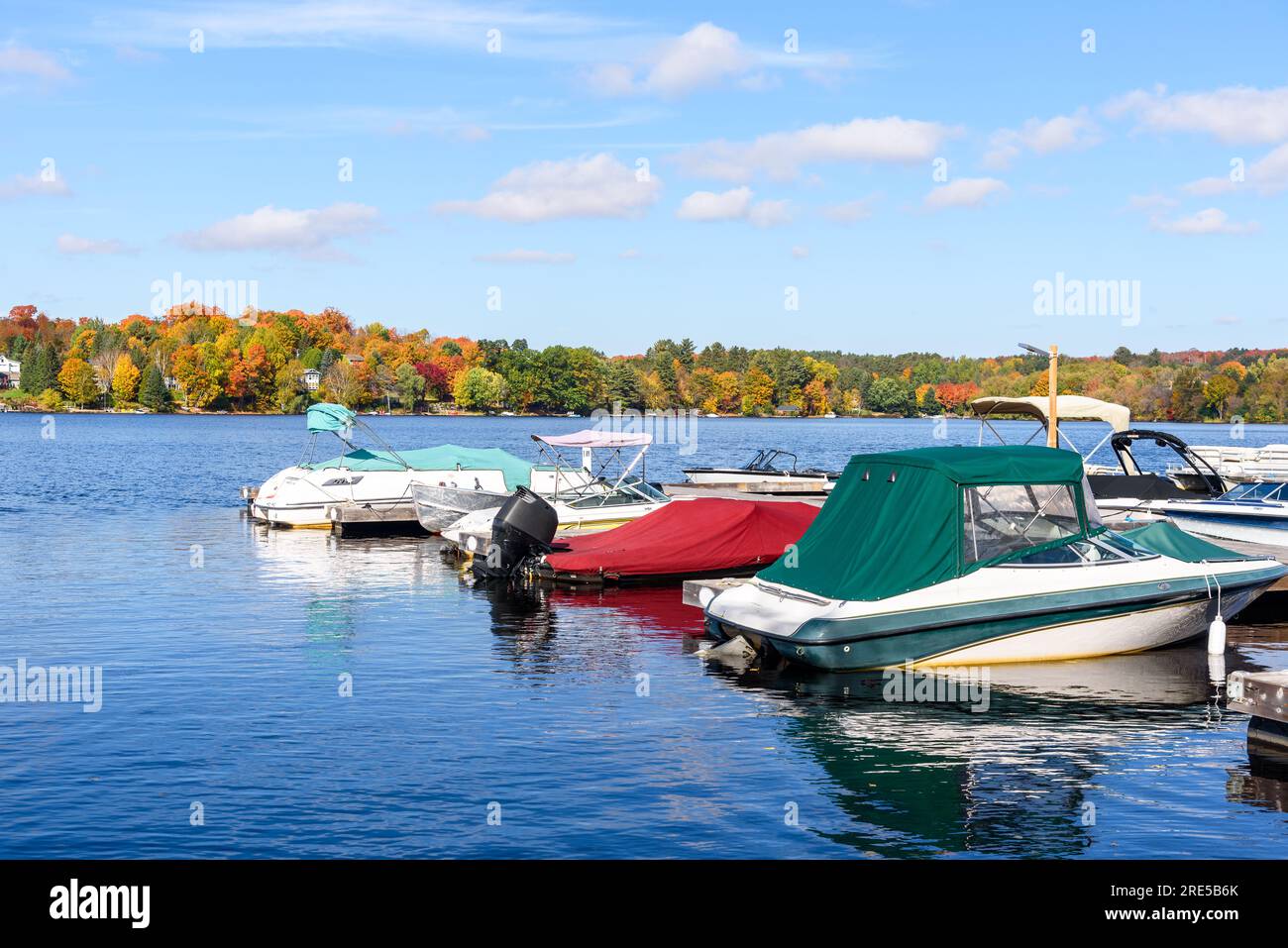 Boote, die an hölzernen Stegen in einem kleinen Hafen an einem See gefesselt sind, umgeben von Wäldern auf dem Gipfel der Herbstfarben Stockfoto
